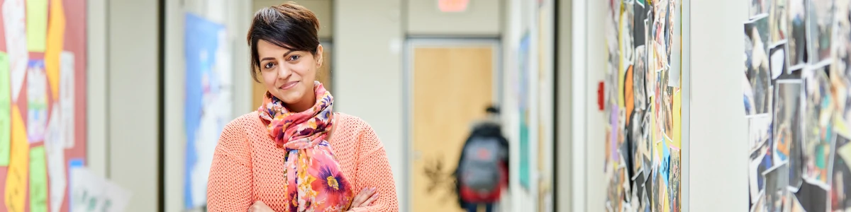 Teacher standing in a school hallway with a student in the background